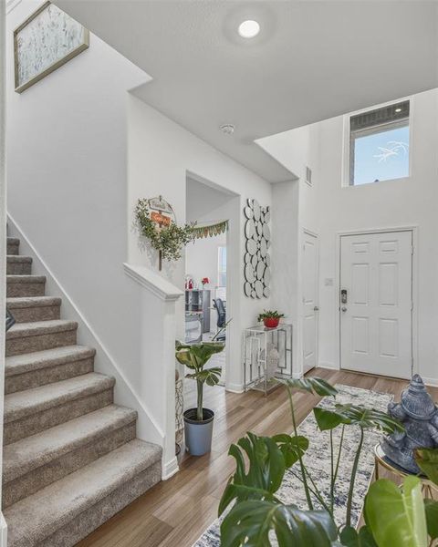 Two-story entryway featuring wood-finish flooring, a white panel door, and high ceilings with an upper-level window Two-story entryway featuring wood-finish flooring, a white panel door, and high ceilings with an upper-level window