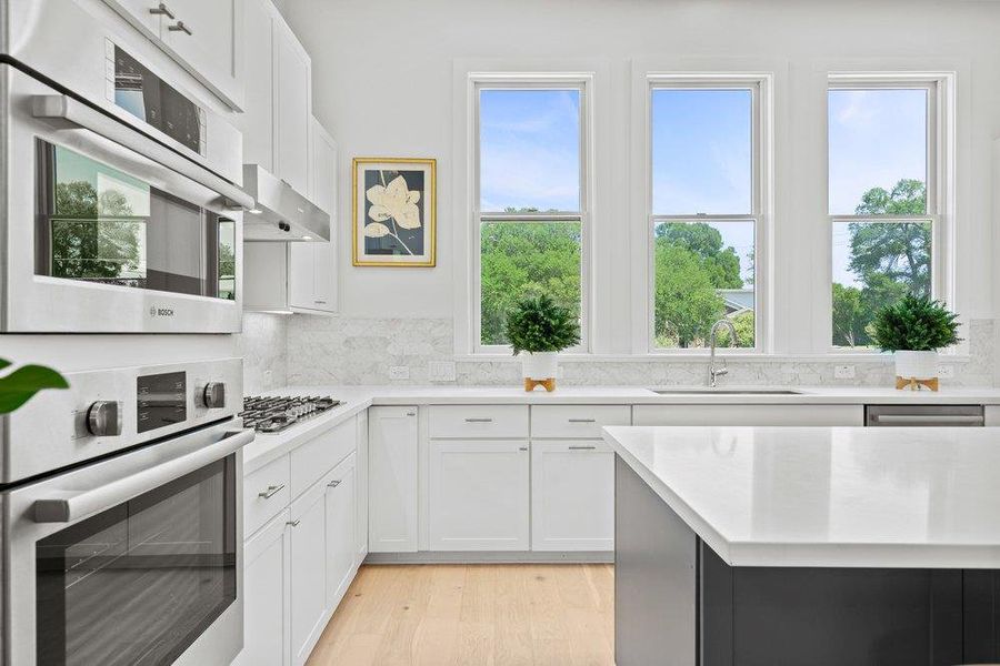 Modern chef’s kitchen featuring sleek quartz countertops, custom cabinetry, Bosh stainless steel appliances, and expansive picture windows.