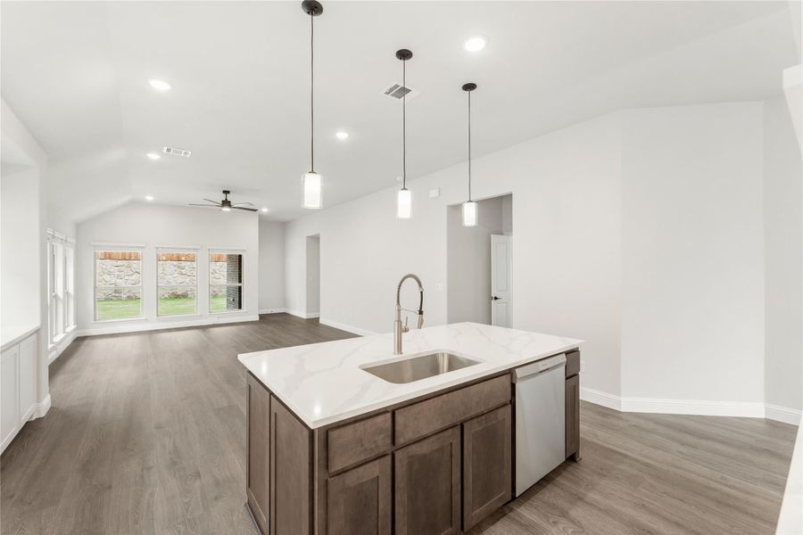 Kitchen island with quartz countertop, sink, and dishwasher, open to living area with vaulted ceiling and hardwood floors Kitchen island with quartz countertop, sink, and dishwasher, open to living area with vaulted ceiling and hardwood floors