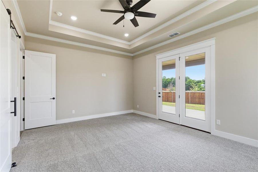 Spacious room featuring light gray carpeting, a tray ceiling with recessed lighting and a ceiling fan, and white French doors opening to the exterior