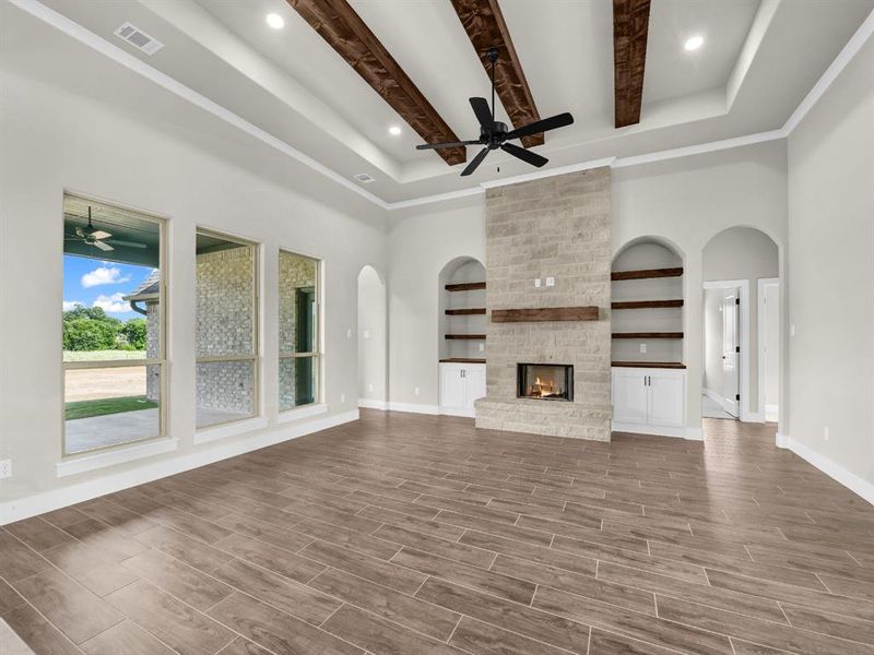 Unfurnished living room with arched walkways, ceiling fan, beam ceiling, wood finish floors, and a fireplace Unfurnished living room with arched walkways, ceiling fan, beam ceiling, wood finish floors, and a fireplace