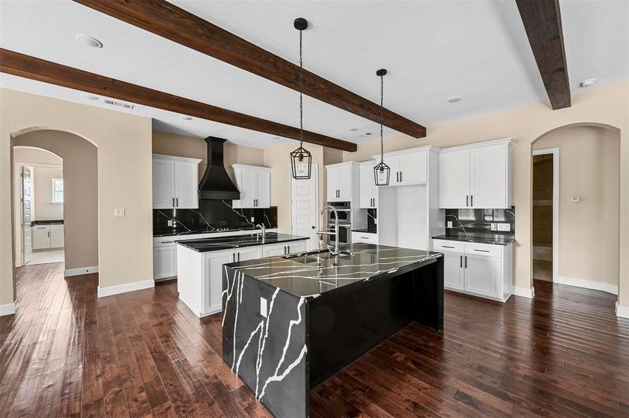 Kitchen with custom exhaust hood, dark hardwood / wood-style flooring, an island with sink, beam ceiling, and backsplash