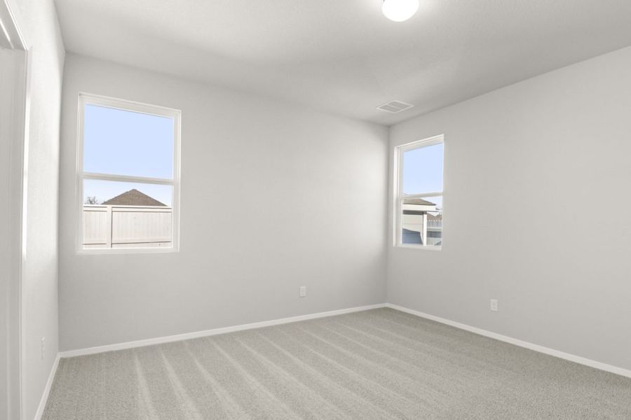 Image of a primary bedroom with tan carpeting and light grey walls with two windows in the corner of the room