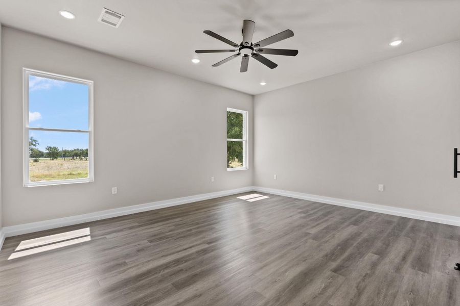 A generously sized room features durable wood-look flooring and multiple windows framing scenic outdoor vistas. A generously sized room features durable wood-look flooring and multiple windows framing scenic outdoor vistas.