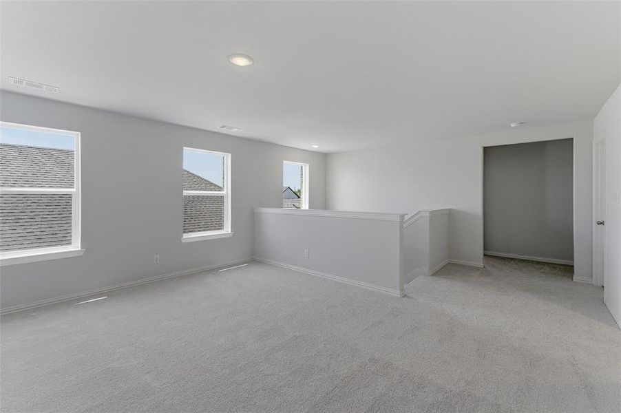 Spacious carpeted open area featuring multiple windows, recessed lighting, neutral wall tones, white trim, and a white railing