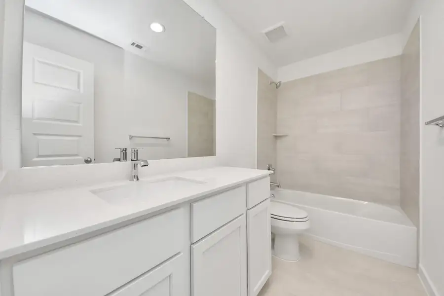 Secondary bath features tile flooring, bath/shower combo with tile surround, light stained wood cabinets, beautiful light countertop.