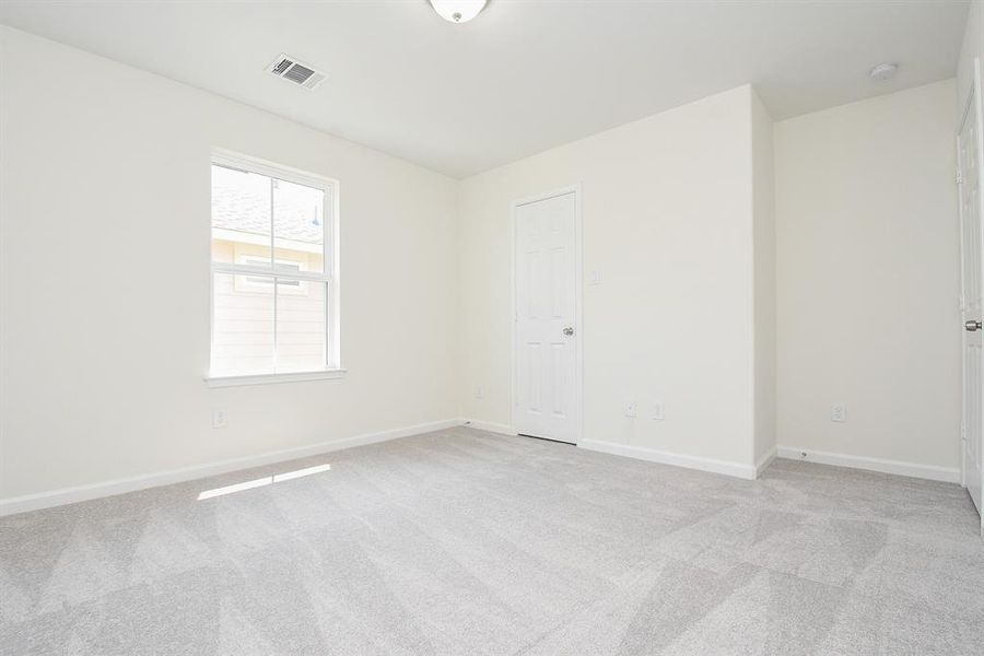 Empty room with carpeted floor, one window, white walls, and a closed door. Bright and clean space.