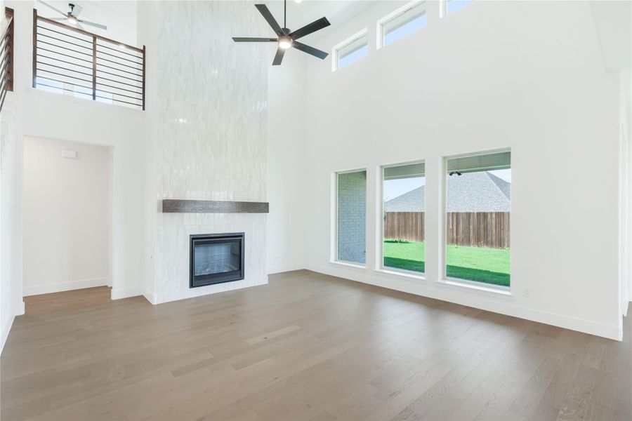 Open living room with two-story ceiling, tile fireplace, hardwood floors, and large windows overlooking backyard