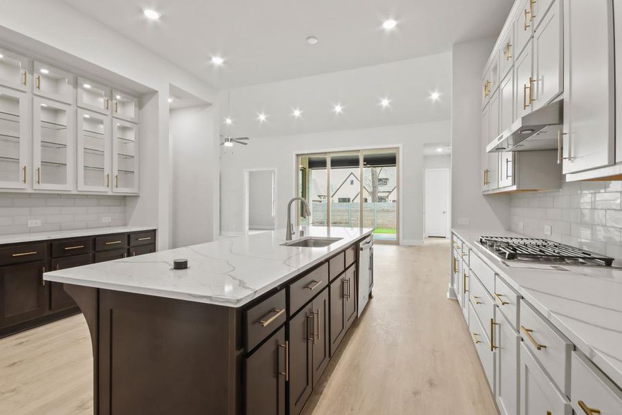 Kitchen featuring stainless steel gas cooktop, a sink, under cabinet range hood, a kitchen island with sink, and light wood-style floors Kitchen featuring stainless steel gas cooktop, a sink, under cabinet range hood, a kitchen island with sink, and light wood-style floors