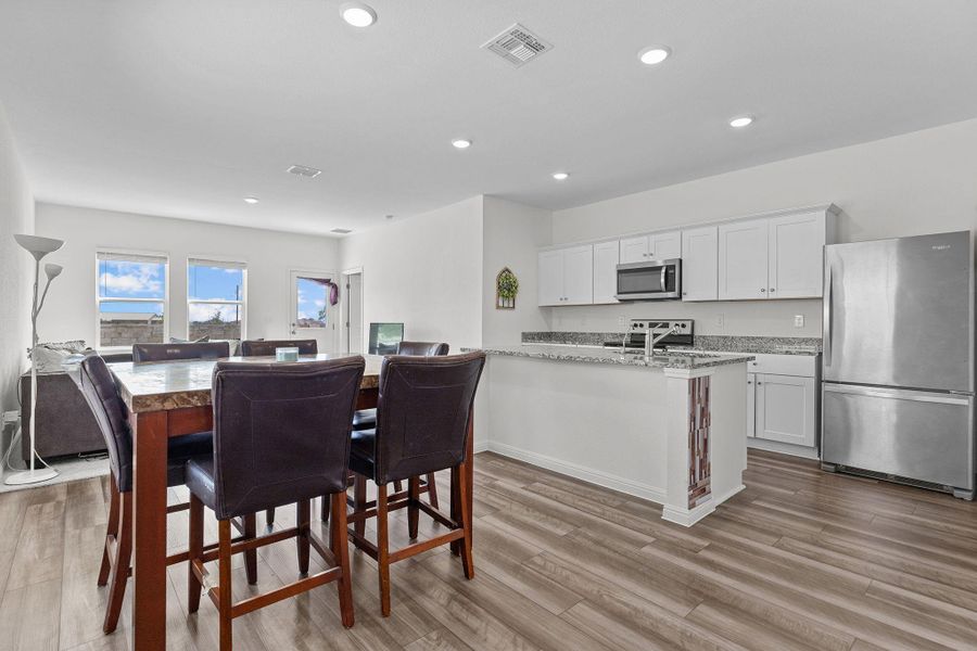 Kitchen featuring appliances with stainless steel finishes, white cabinetry, light wood finished floors, recessed lighting, and light stone countertops Kitchen featuring appliances with stainless steel finishes, white cabinetry, light wood finished floors, recessed lighting, and light stone countertops