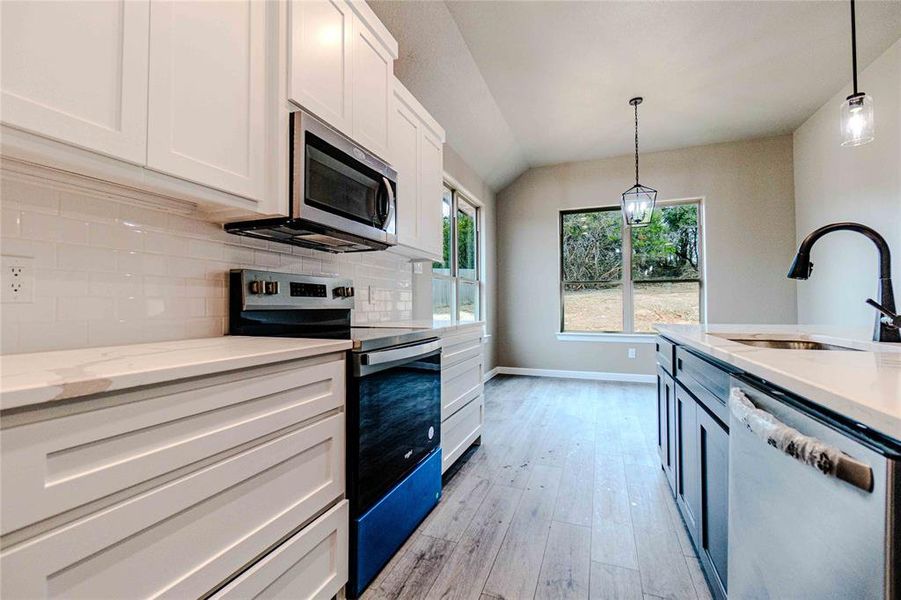 Kitchen with appliances with stainless steel finishes, sink, white cabinets, and decorative light fixtures