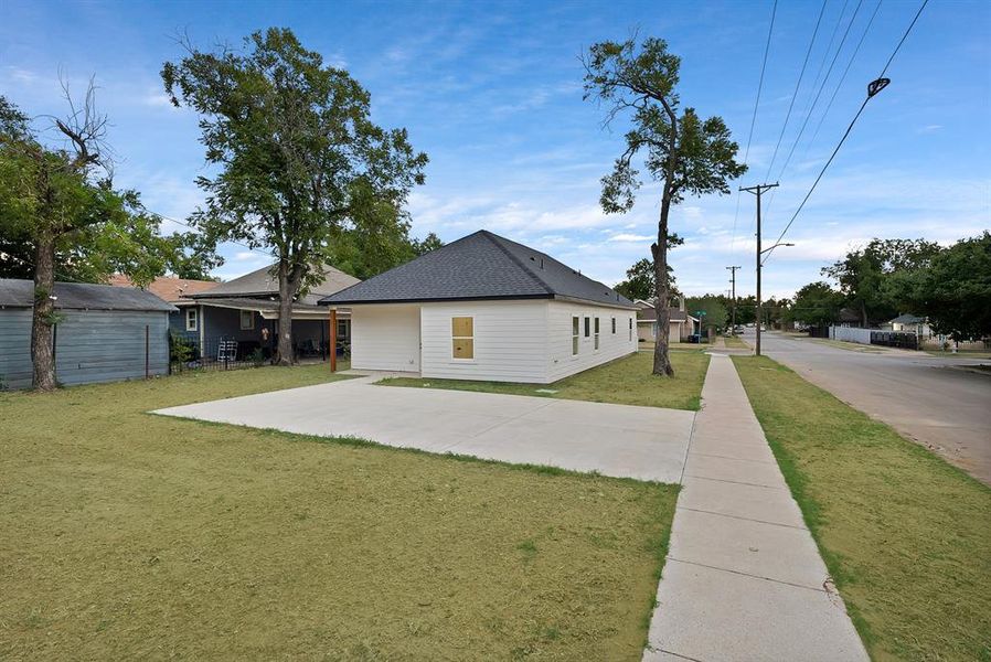 View of side of property with a yard, a shingled roof, and a patio area
