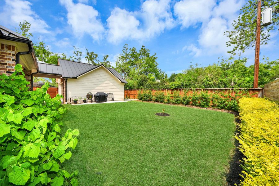 This photo showcases a spacious, well-maintained backyard with lush green grass, a patio area with seating, and vibrant landscaping, providing a private and serene outdoor space.