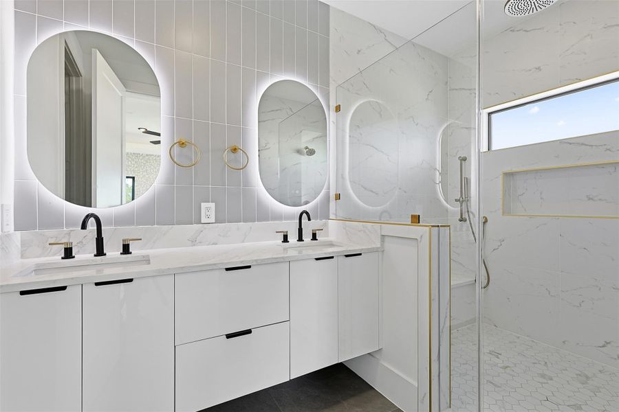 Same floorplan - different finishes. The Primary Bathroom equipped with dual-sink vanity includes flat-panel cabinetry, matte black faucets, and twin oval mirrors with integrated LED perimeter lighting.