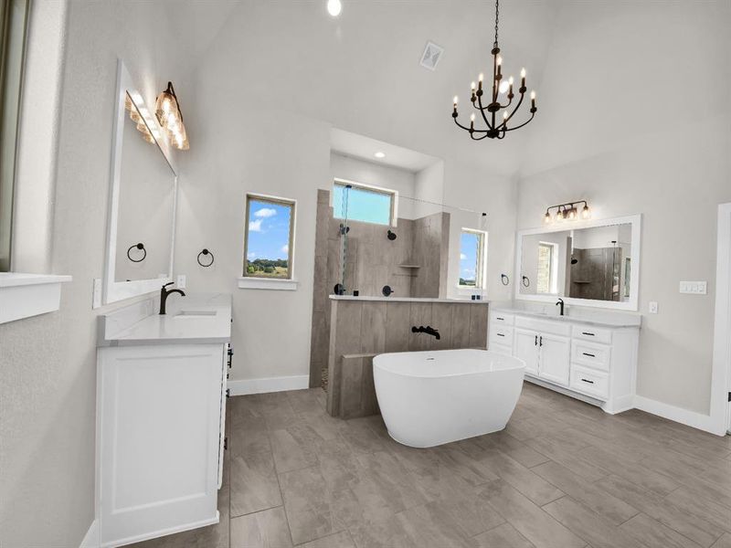 Bathroom with two vanities, walk in shower, a freestanding tub, and a chandelier