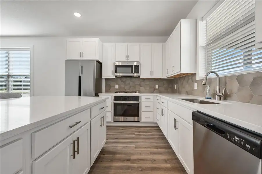 Kitchen features beautiful granite, white cabinetry with soft close doors and adjustable shelving, appliances with stainless steel finishes, LVP wood-type flooring, ceramic backsplash, and recessed lighting.