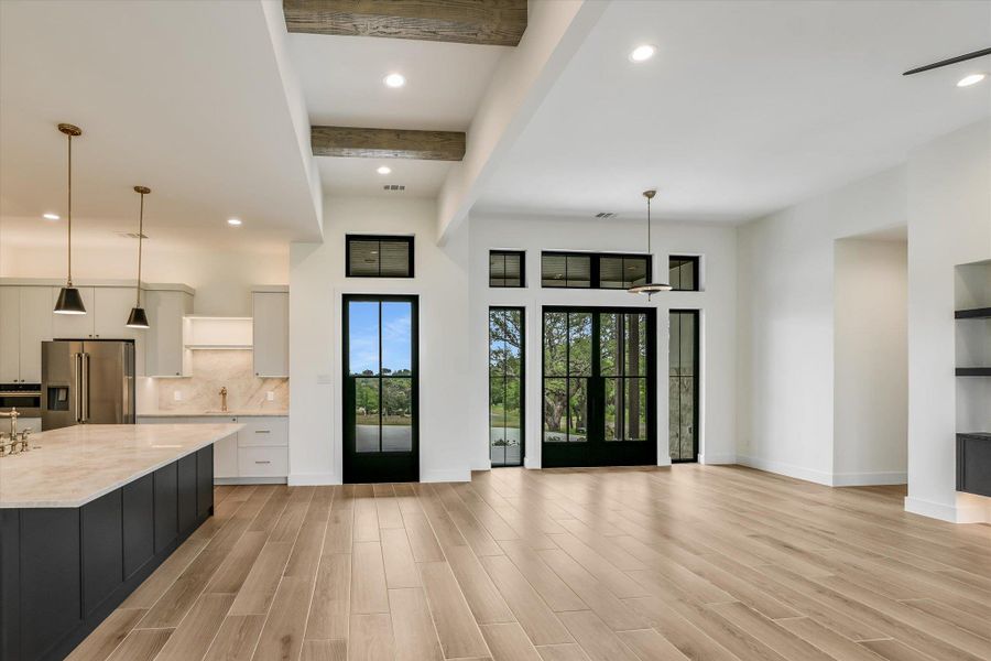 Spacious open-concept living area featuring wood-finish flooring, vaulted ceilings with exposed beams, and recessed lighting