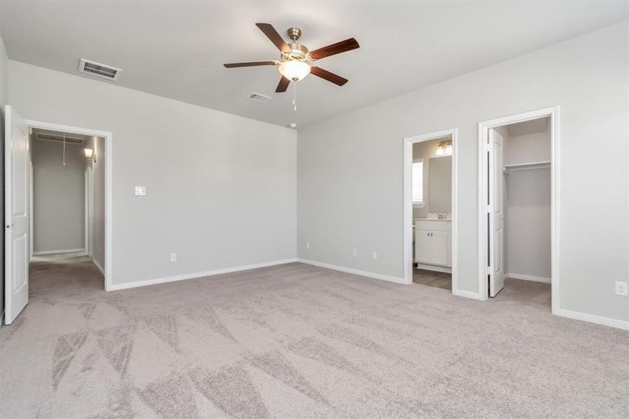 The expansive primary bedroom is a true retreat, offering ample space for rest and relaxation. With plush carpeting, a ceiling fan for added comfort, and multiple access points to the en-suite bathroom and walk-in closet, this room is designed with your comfort in mind. The neutral color palette creates a serene atmosphere, perfect for unwinding at the end of the day. **This image is from another Saratoga Home with similar floor plan and finishes, not the June floorplan.**