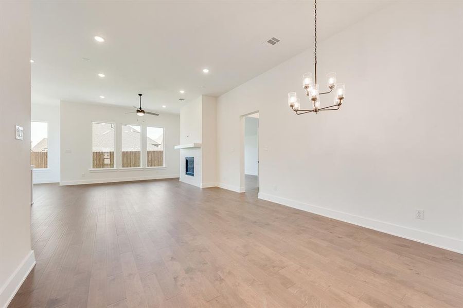 Unfurnished living room featuring a glass covered fireplace, recessed lighting, light wood-style floors, a chandelier, and a ceiling fan Unfurnished living room featuring a glass covered fireplace, recessed lighting, light wood-style floors, a chandelier, and a ceiling fan