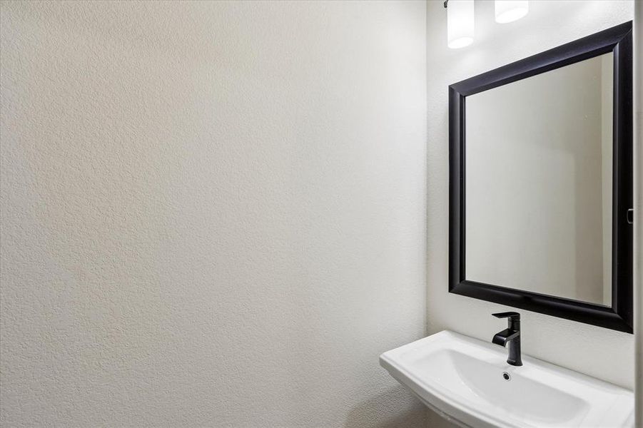 Modern wall-mounted sink with a matte black faucet, framed mirror, and contemporary vanity lighting Modern wall-mounted sink with a matte black faucet, framed mirror, and contemporary vanity lighting