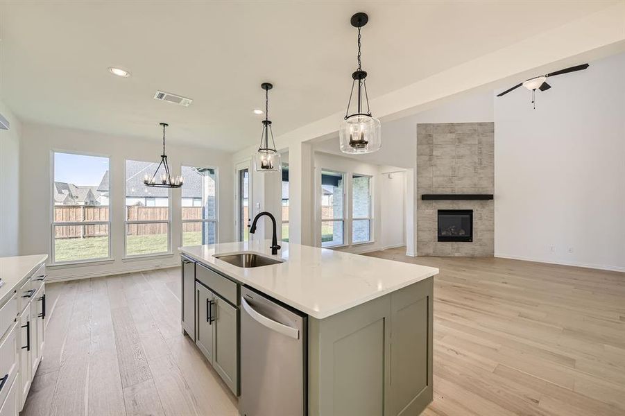 Kitchen with an island with sink, light hardwood / wood-style flooring, dishwasher, decorative light fixtures, and sink