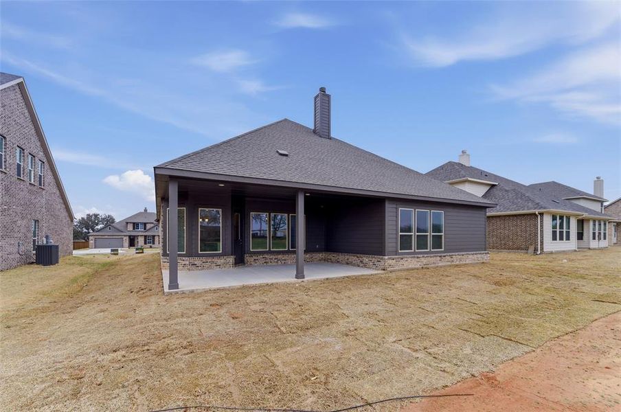 Back of property with a shingled roof, a patio, a chimney, and a lawn