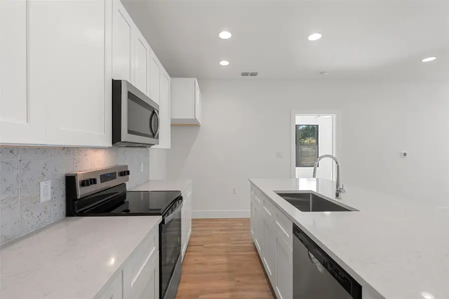 Kitchen featuring appliances with stainless steel finishes, recessed lighting, white cabinetry, light wood finished floors, and light stone counters