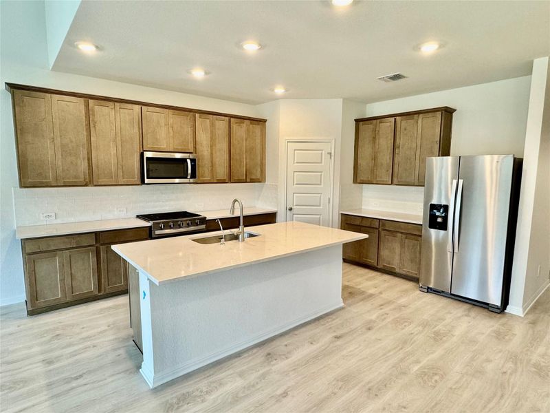 Kitchen with stainless steel appliances, recessed lighting, an island with sink, tasteful backsplash, and light wood-style flooring Kitchen with stainless steel appliances, recessed lighting, an island with sink, tasteful backsplash, and light wood-style flooring