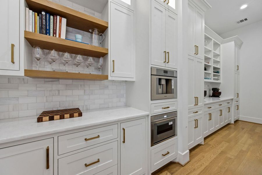 Alternate view showcasing custom shaker cabinetry, built-in coffee station, and integrated appliances. Open shelving with wood accents adds warmth, while under-cabinet lighting and thoughtful storage enhance both style and function.