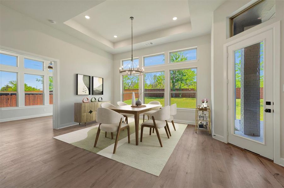 Dining area with light wood-type flooring, hanging lights, and a tray ceiling