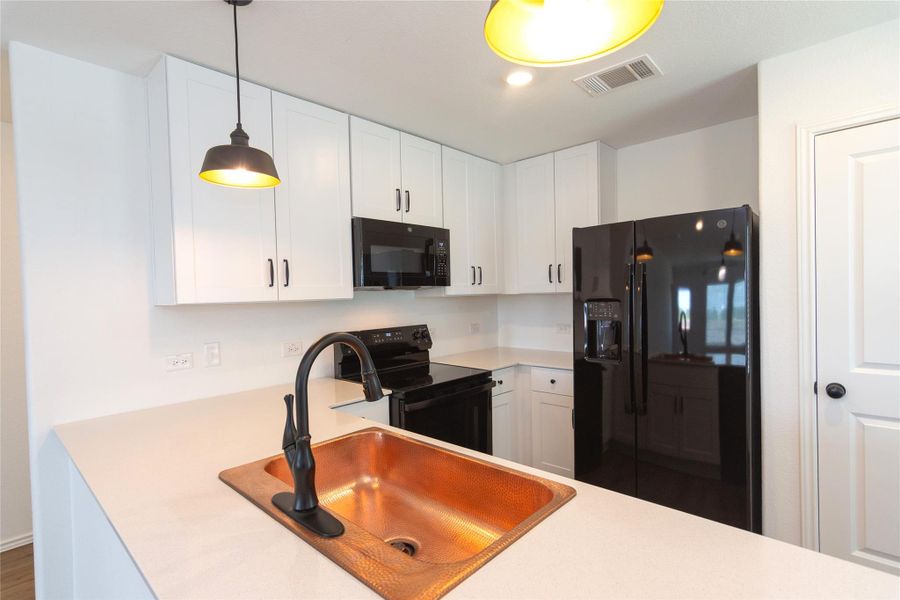 Kitchen featuring white shaker-style cabinetry, a copper sink, a pull-down faucet, white countertops, and black appliances