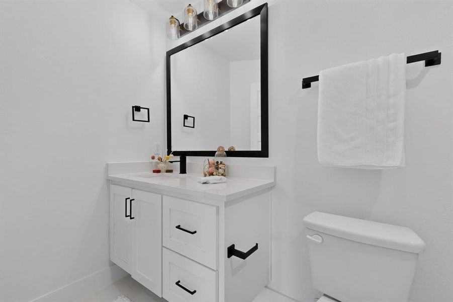 Modern bathroom featuring a white vanity with shaker-style cabinetry, a stone-finish countertop, and a rectangular mirror with a black frame