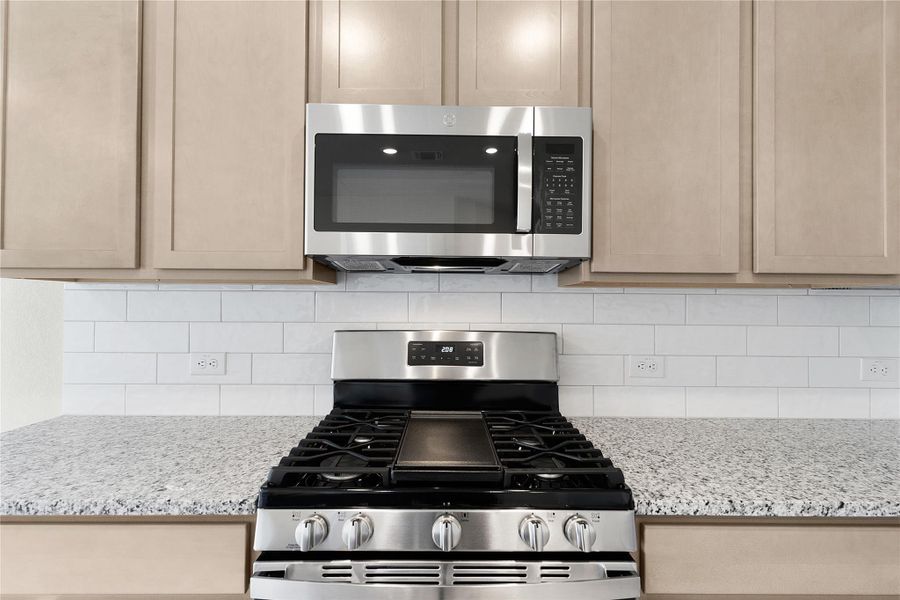 Kitchen featuring stainless steel appliances, light stone counters, light wood finish cabinets, and tasteful backsplash