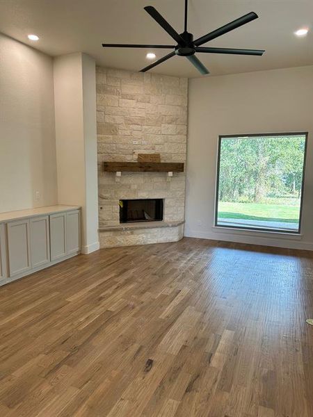 Unfurnished living room with a stone fireplace, ceiling fan, wood finished floors, and recessed lighting