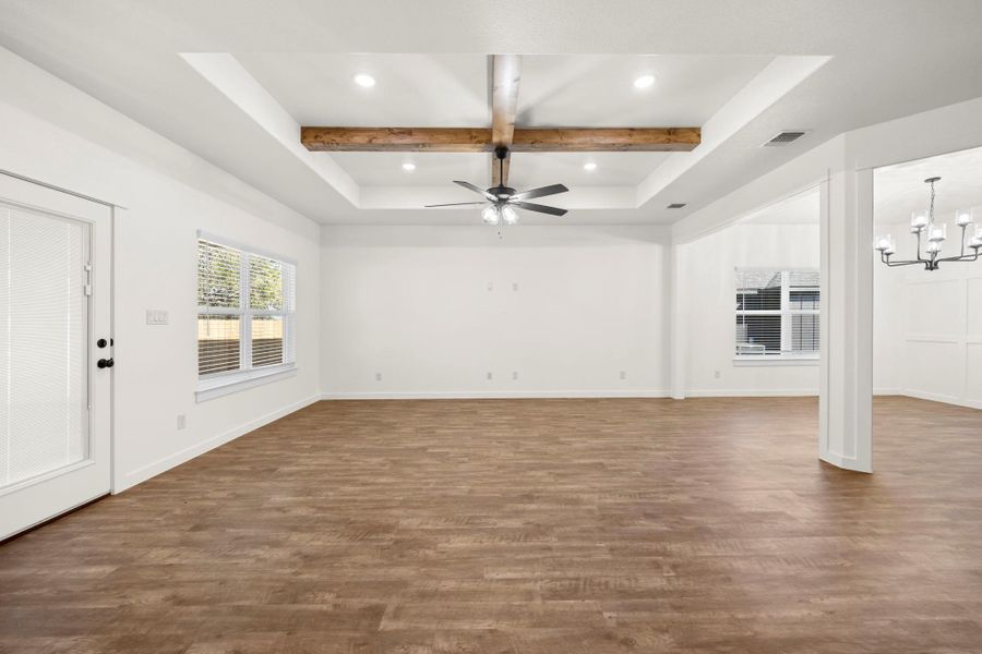 An airy living space features a stylish ceiling fan and a beautiful tray ceiling with wooden beams.