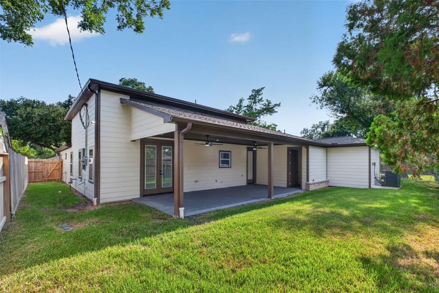 Spacious backyard with a covered patio perfect for outdoor entertaining, surrounded by lush greenery and a wooden privacy fence.