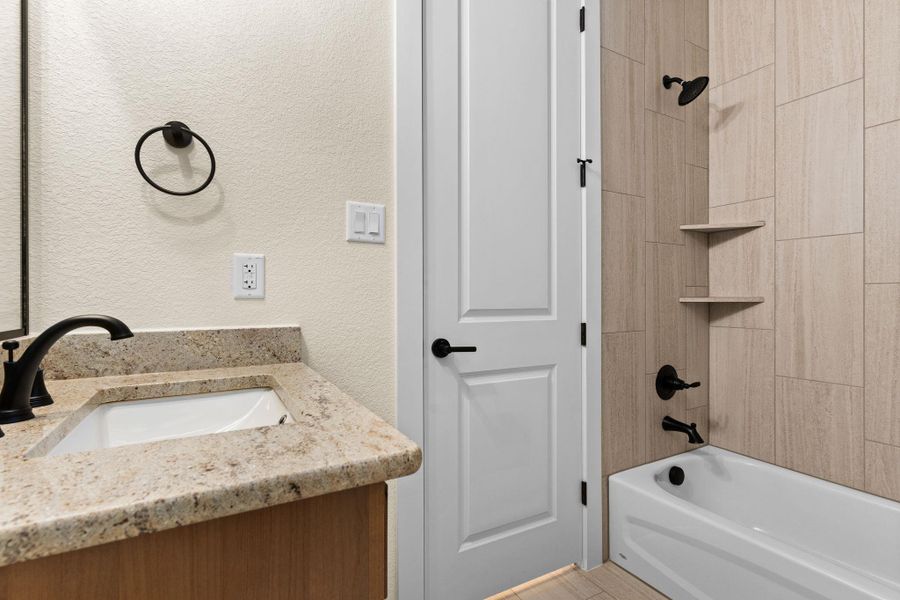 Bathroom featuring a textured wall, vanity, and washtub / shower combination Bathroom featuring a textured wall, vanity, and washtub / shower combination
