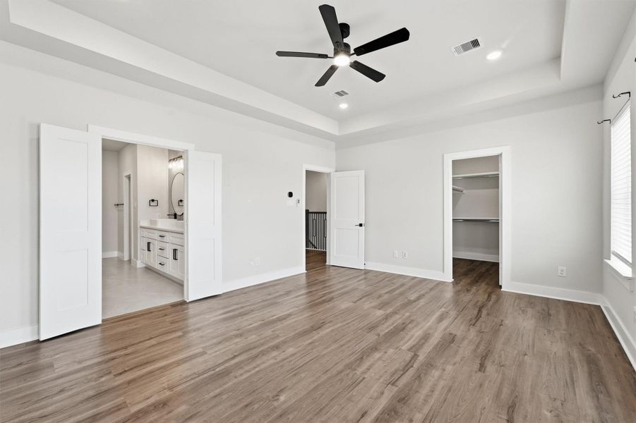 Spacious primary suite featuring a tray ceiling, wide-plank flooring, dual walk-in closets, and a luxurious ensuite bath with modern finishes.