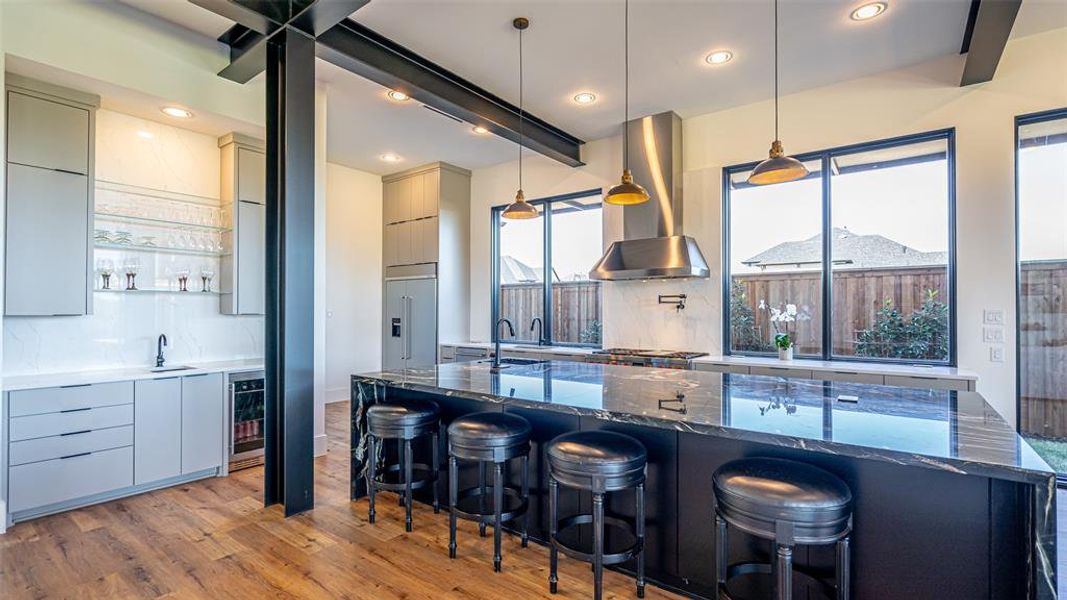 Kitchen with dark stone counters, decorative light fixtures, wall chimney exhaust hood, and a breakfast bar area