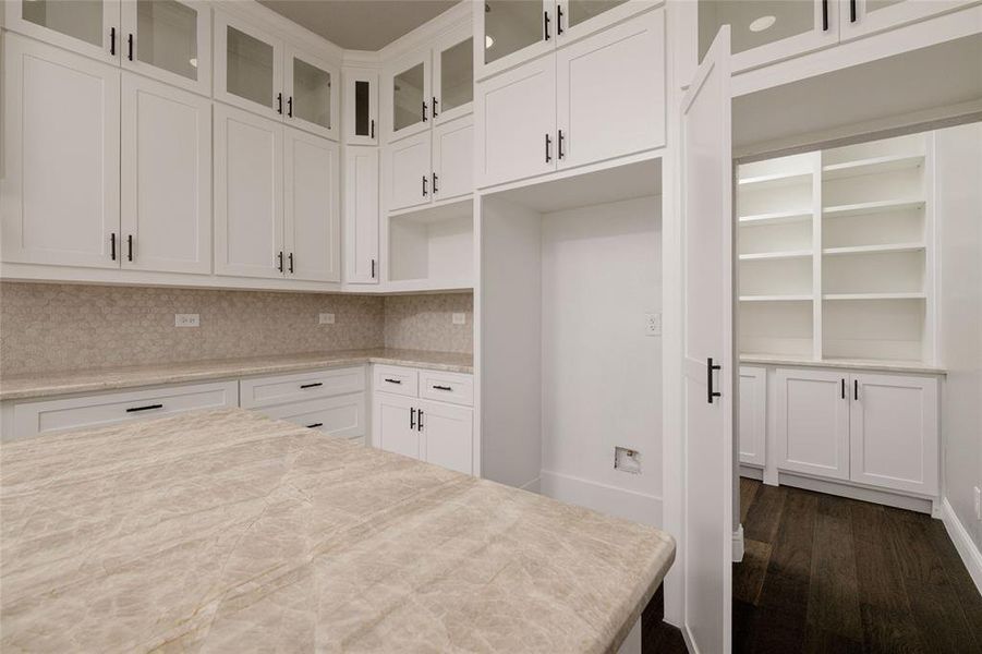 Kitchen with white cabinetry, decorative backsplash, dark wood-style floors, and glass insert cabinets Kitchen with white cabinetry, decorative backsplash, dark wood-style floors, and glass insert cabinets