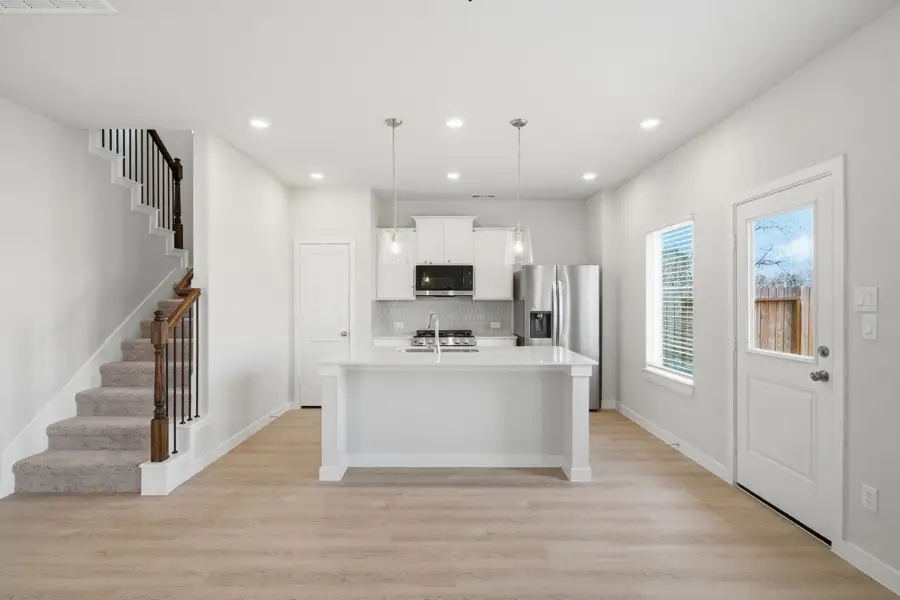 A large kitchen with a large white counter and a white staircase. A large kitchen with a large white counter and a white staircase.