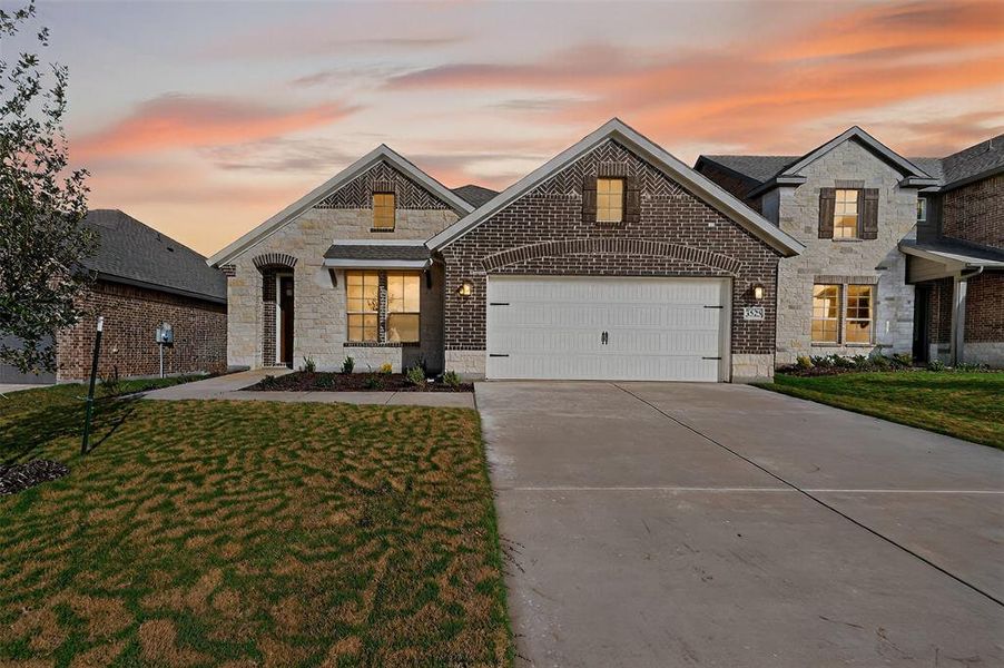 French country style house featuring stone siding, a yard, brick siding, concrete driveway, and an attached garage