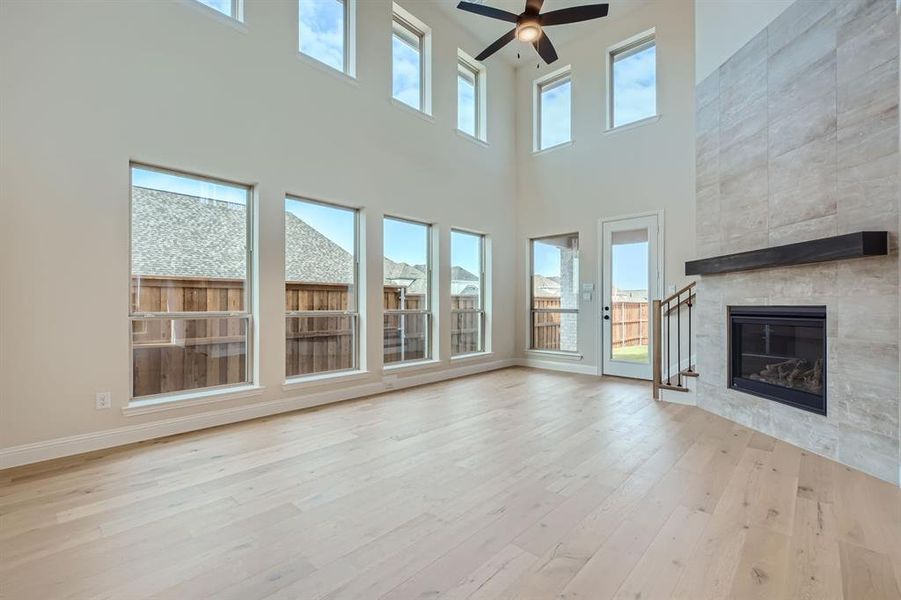 Unfurnished living room featuring a healthy amount of sunlight, a tile fireplace, light wood-type flooring, and ceiling fan