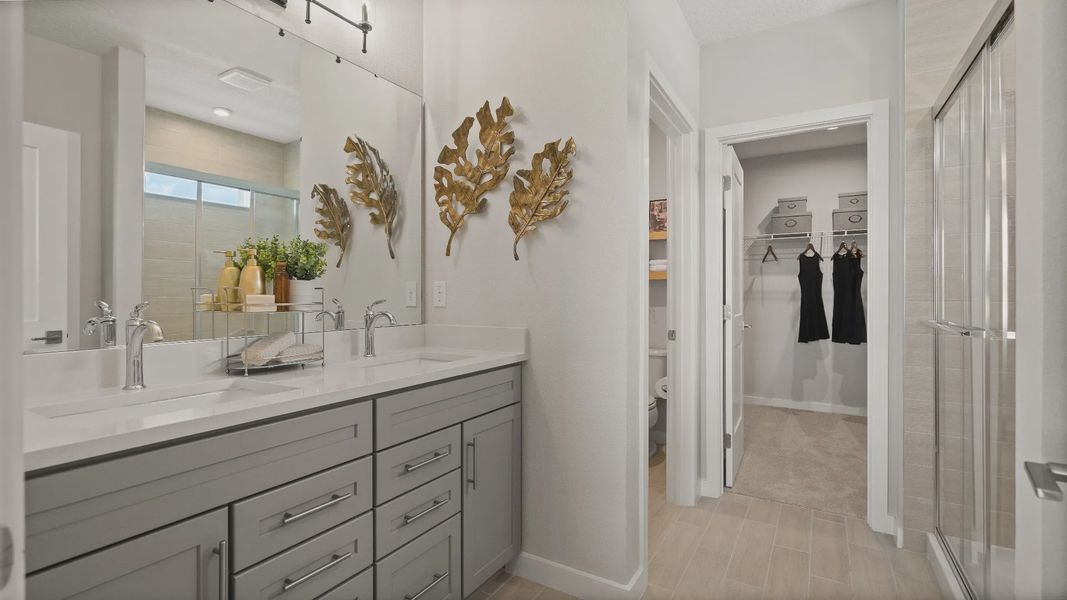 Modern owner’s bath in the Jupiter Model at Grasslands West,  featuring dual vanity sinks, glass shower, and walk-in closet.