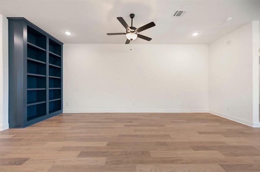 The room features light-colored flooring, a ceiling fan with integrated lighting, recessed lighting, and a built-in dark blue bookshelf