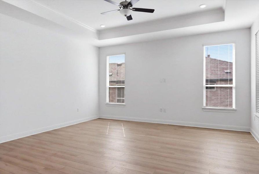 A tranquil primary bedroom with light wood flooring and elevated tray ceilings awaits. A tranquil primary bedroom with light wood flooring and elevated tray ceilings awaits.