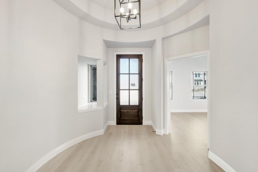 Round foyer with wood glass-panel front door, tray ceiling, pendant light, and light hardwood floors