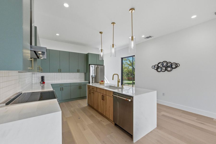 Kitchen with light stone countertops, light wood-style flooring, appliances with stainless steel finishes, backsplash, and decorative light fixtures