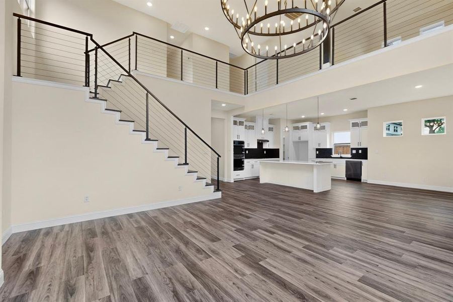 Open-concept living area featuring wood-finish flooring, a contemporary staircase with cable railing, and high ceilings