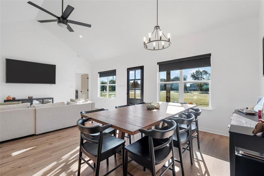 Dining space with light wood-style floors, high vaulted ceiling, recessed lighting, a ceiling fan, and a chandelier